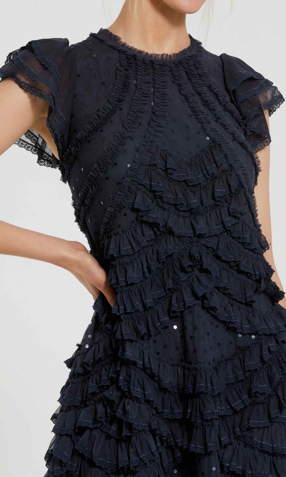 A person is wearing the Mac Duggal 8371 Midi Party Dress, a short-sleeve black dress designed with sheer fabric, textured polka dots, and layered ruffles with delicate micro-ruffle detailing. Only the upper body is visible against a plain light background.